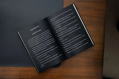 Open book on a wooden surface with black pages and white text.