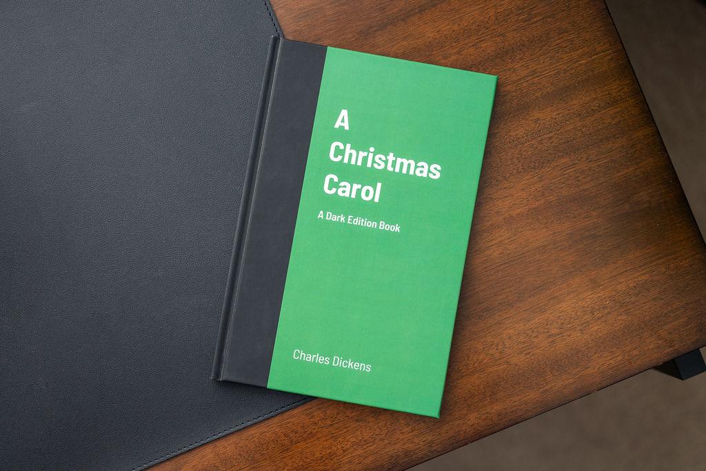 Green book titled 'A Christmas Carol' by Charles Dickens on a wooden surface.