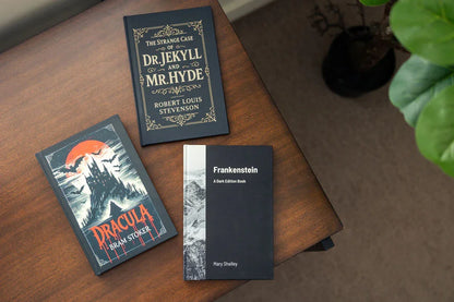 Three books on a wooden surface: 'Dracula', 'The Strange Case of Dr. Jekyll and Mr. Hyde', and 'Frankenstein'.